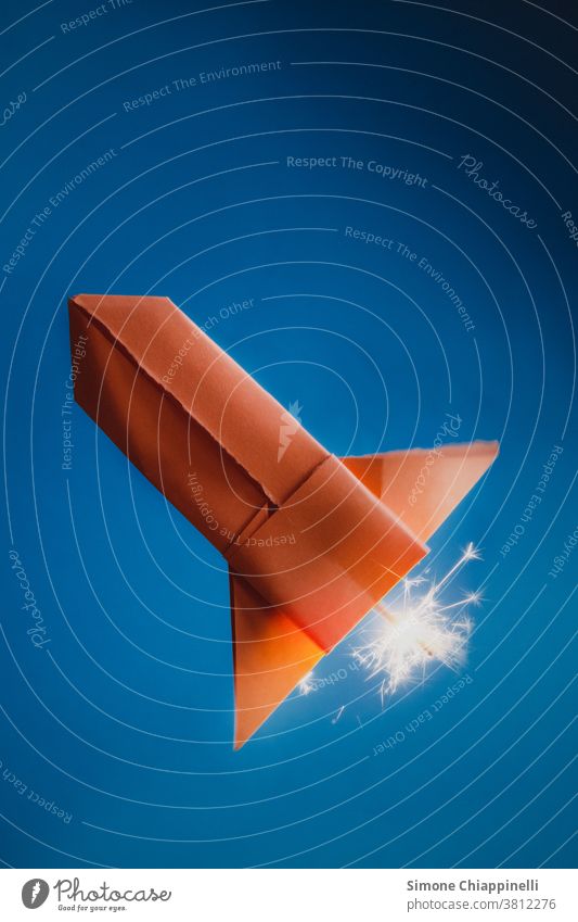 Orange origami paper rocket on blue background space rocket Blue sky Origami Paper Colour photo Handicraft Creativity Leisure and hobbies Interior shot