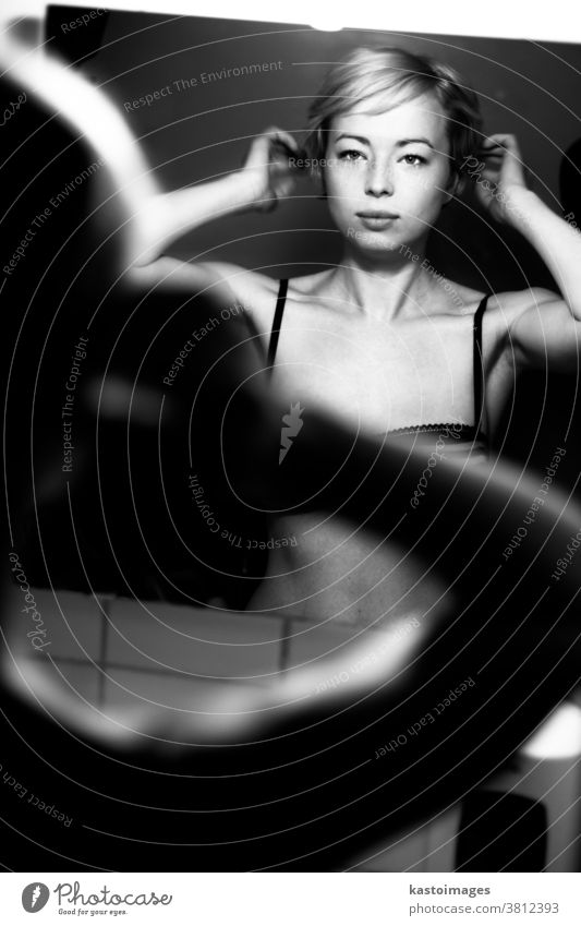 Woman getting ready for work doing morning makeup routine applying make up and doing her hair in front of bathroom mirror at home. Black and white image.