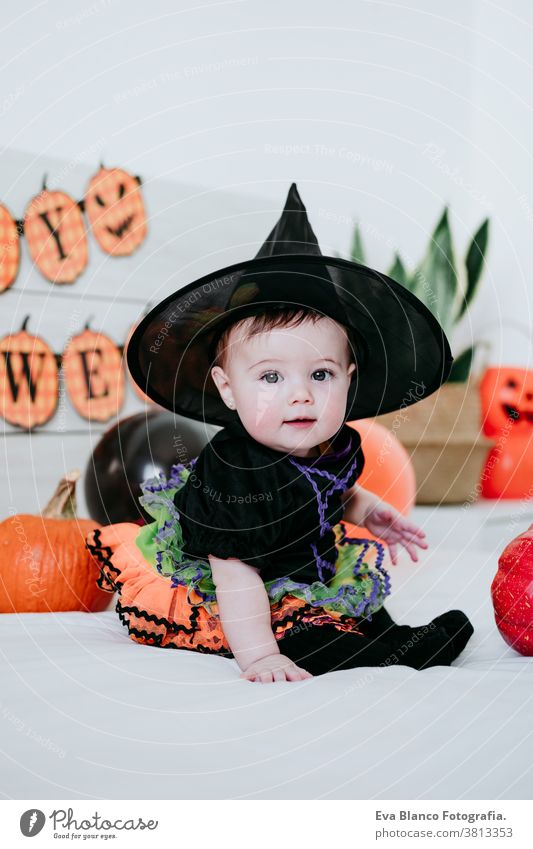 beautiful baby girl in witch halloween costume at home, sitting on bed with Halloween decoration, Lifestyle indoors trick or treat pumpkin balloons orange