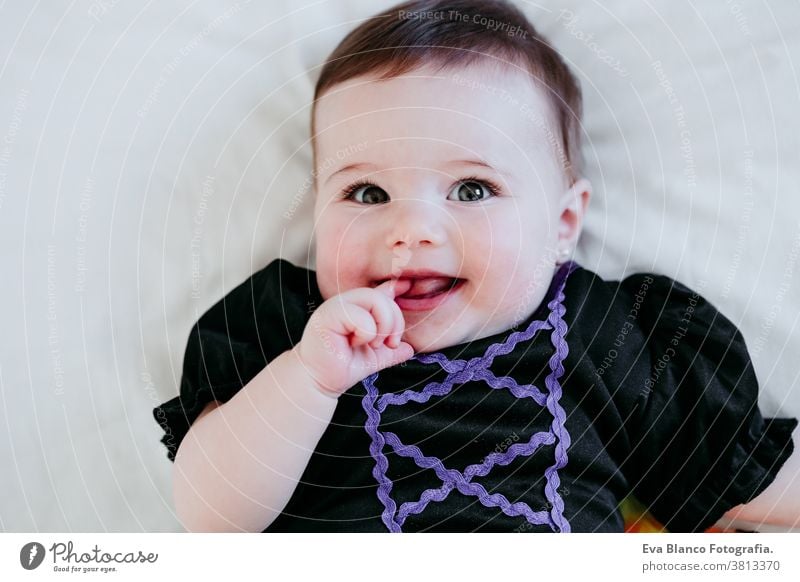 beautiful baby girl in witch halloween costume at home, sitting on bed with Halloween decoration, Lifestyle indoors trick or treat pumpkin balloons orange