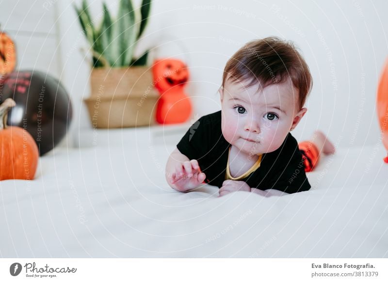 beautiful baby girl in halloween costume at home, sitting on bed with Halloween decoration, Lifestyle indoors trick or treat pumpkin balloons orange october