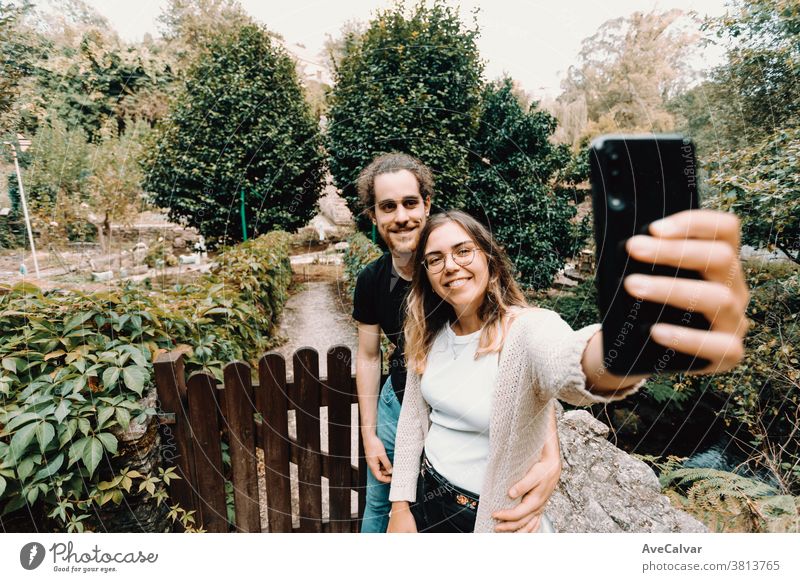 Young and smiling couple taking a selfie in front of a beautiful rural house self-portrait fun smart-phone lifestyle summer together love male man smile park