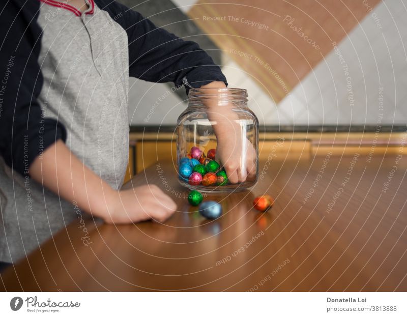 child takes chocolates from the jar at home celebration childhood colored concept craving easter eggs glass jar greed greedy greedy food hand hands kid kitchen