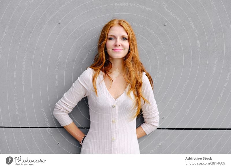 Young redhead woman leaning on grey wall red hair urban dress style positive trendy young female smile confident contemporary fashion content lifestyle