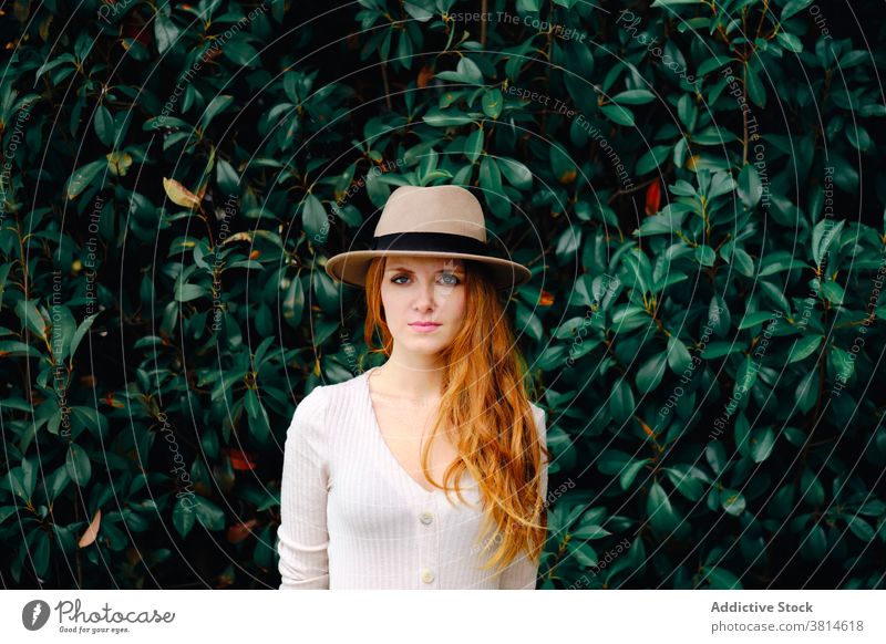 Young woman in hat standing in garden style redhead trendy red hair modern ginger vogue young female fashion long hair lady confident charming lifestyle elegant