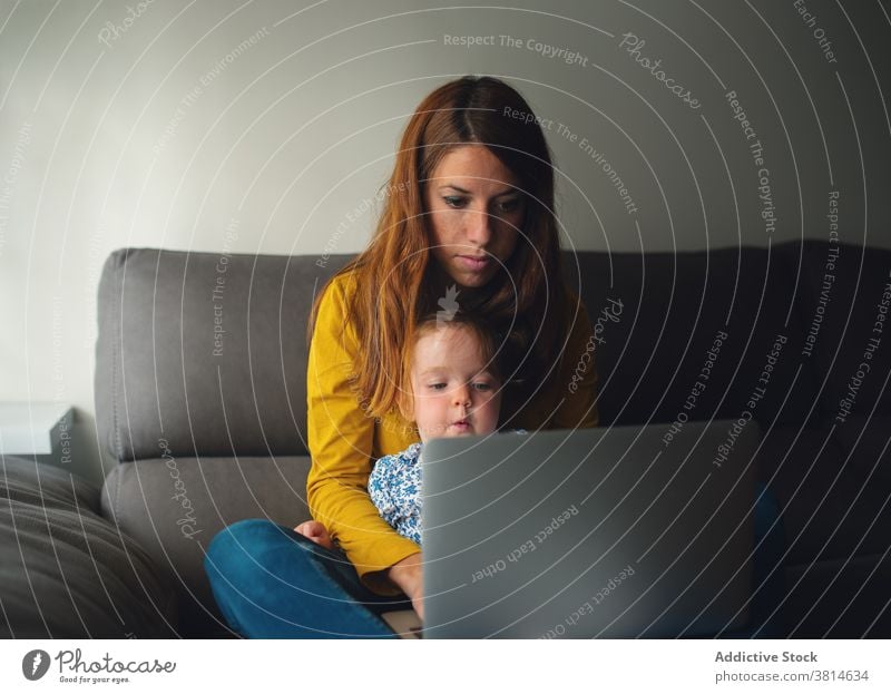 Woman with little kid using laptop at home mother work busy toddler remote daughter child together motherhood gadget device lifestyle mom browsing freelance