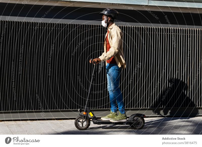 Black man riding scooter in city electric ride mask helmet protect coronavirus vehicle male ethnic black african american medical modern safety urban town sunny