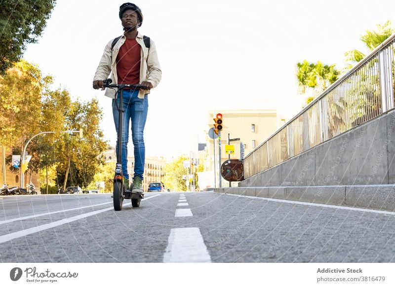 Ethnic man riding electric scooter along crosswalk commute ride city summer road mask male ethnic black african american new normal modern helmet safety urban