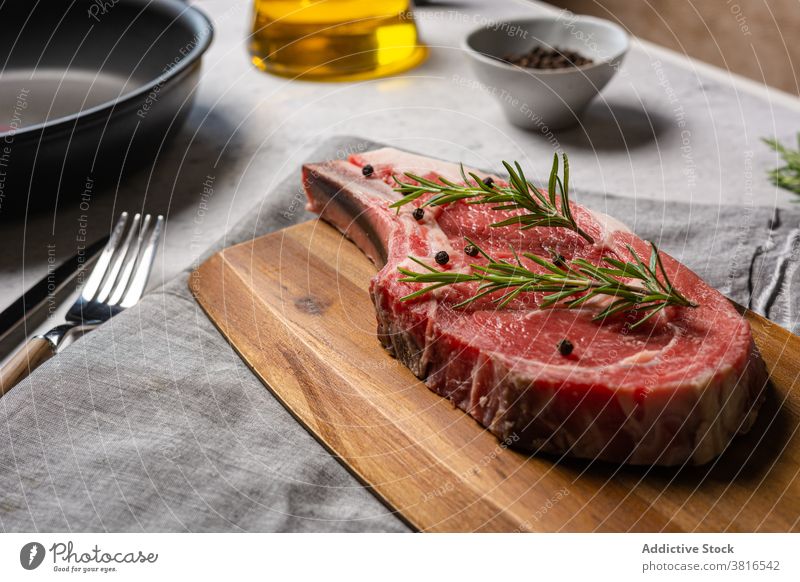 Raw beef steak with herbs on cutting board raw bone t bone rosemary garnish meat pepper black wooden kitchen cook food cuisine delicious dish spice gourmet