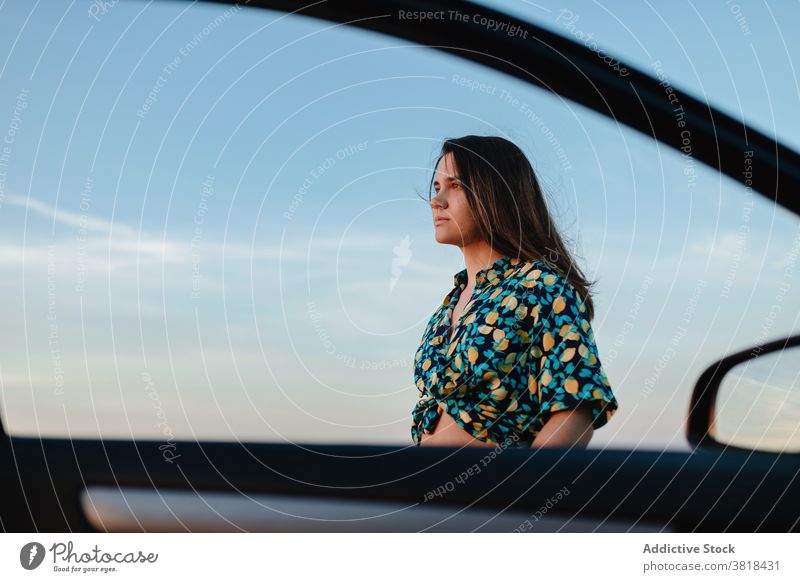 Stylish woman near car door under sky trendy apparel ornament blue sky cloudy charming feminine stylish wear auto mirror atmosphere summer harmony idyllic