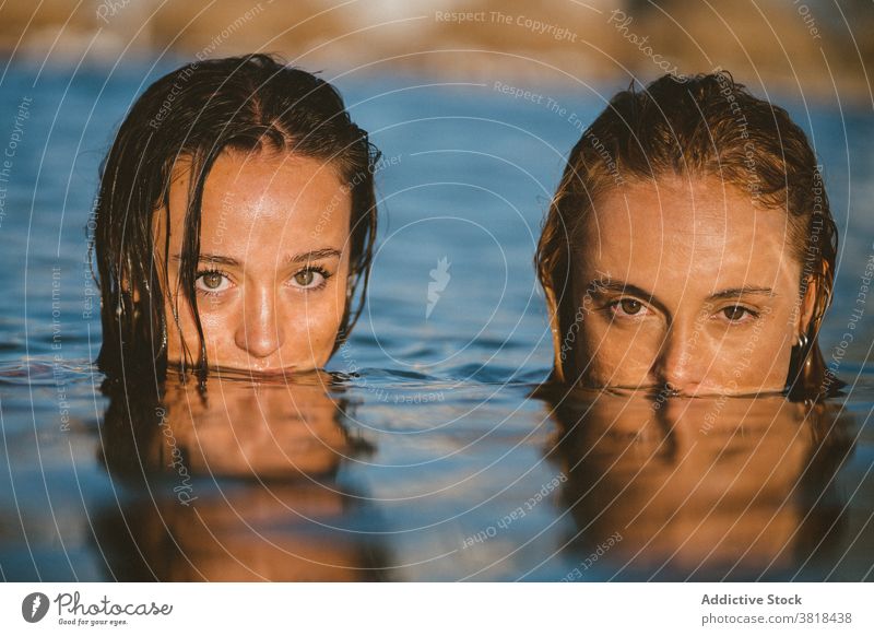 Young women in sea water in summer cover mouth friend together wet hair sunset ocean charming enjoy freedom weekend vacation carefree rest holiday nature