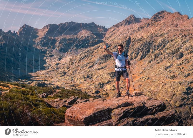 Anonymous tourist taking selfie on smartphone in mountains highland nature vacation mask covid19 using gadget cellphone trekking pole blue sky cloudy traveler