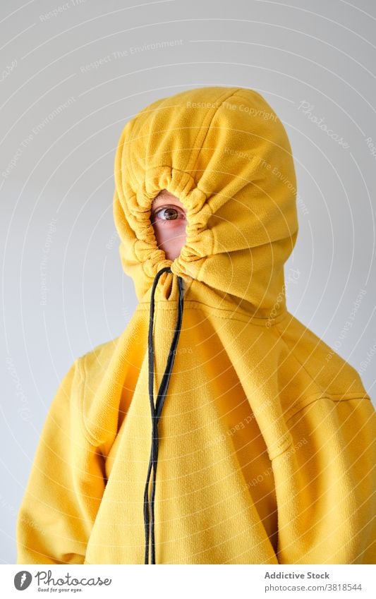 Unrecognizable teen hiding in hood in studio cover hide having fun yellow hoodie teenage style expressive playful childish carefree funny individuality cool