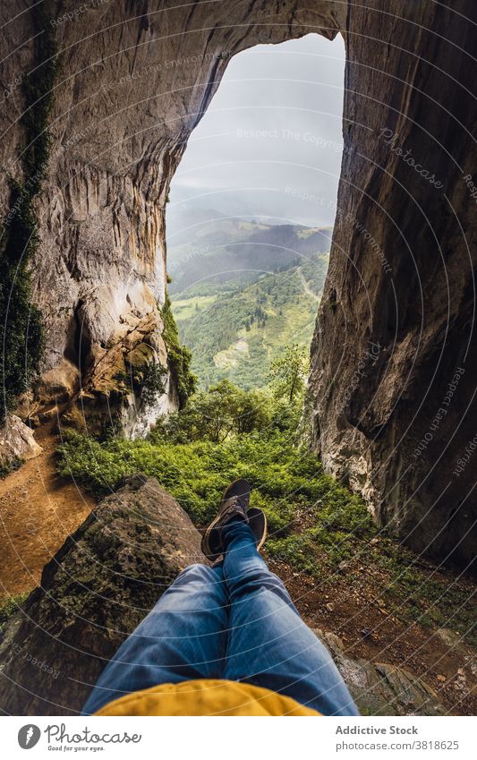 Faceless traveler contemplating cave and mounts during trip contemplate mountain fog nature highland cloudy sky legs crossed moss admire vegetate atmosphere