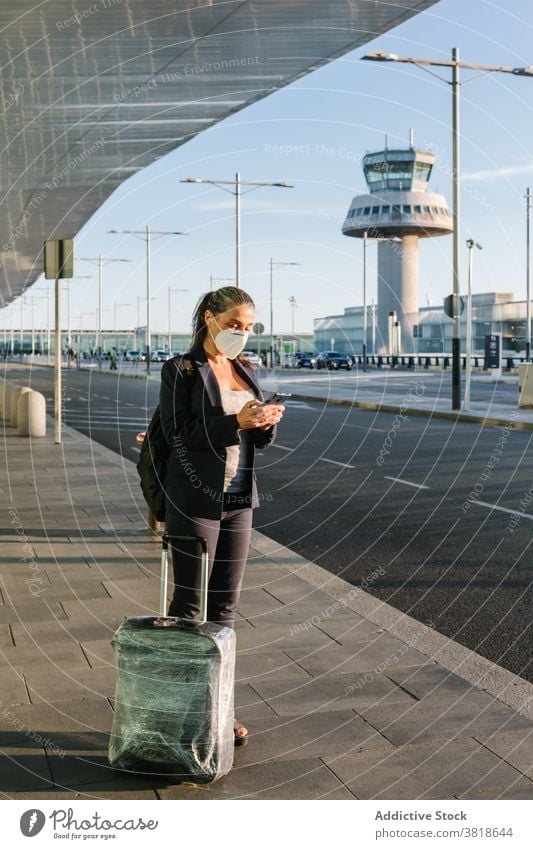 Woman in mask waiting for taxi in airport browsing woman arrive coronavirus protect epidemic traveler smartphone suitcase baggage respirator luggage tourist