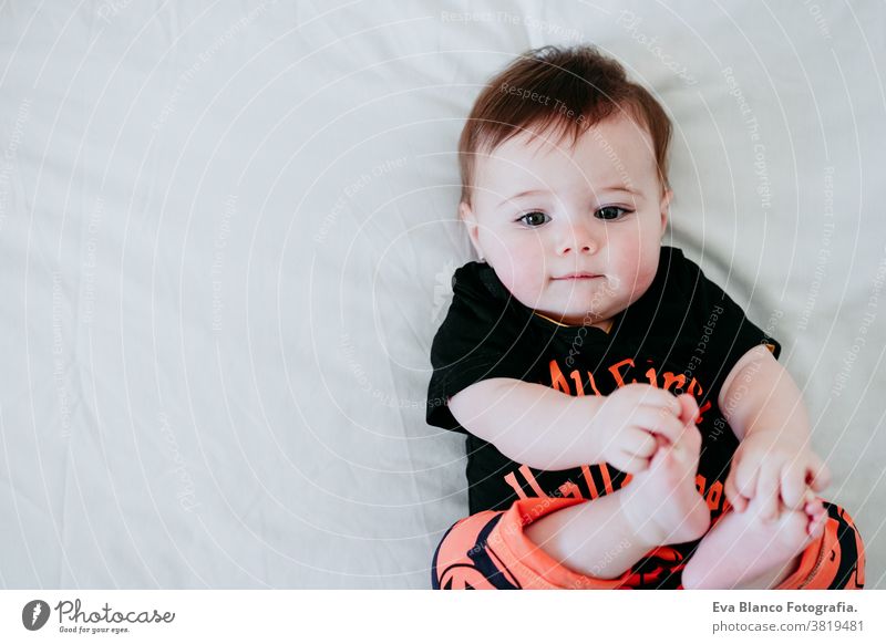 cute baby girl in halloween costume at home, sitting on bed with Halloween decoration, Lifestyle indoors trick or treat pumpkin balloons orange october house