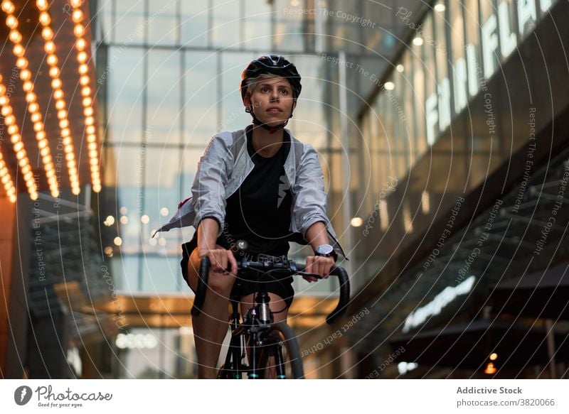 Woman courier cycling near tall building with glass windows in city Cyclist bricked day woman young sports riding summer helmet protective girl delivery