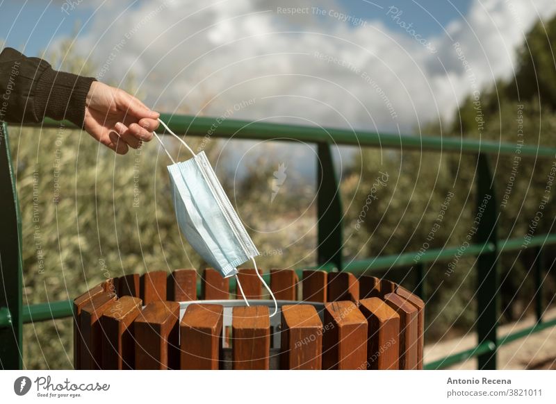 Woman prepares to throw surgical mask in the trash outside a park recycling covid-19 throwing hand basket dirt coronavirus woman outdoors nature people