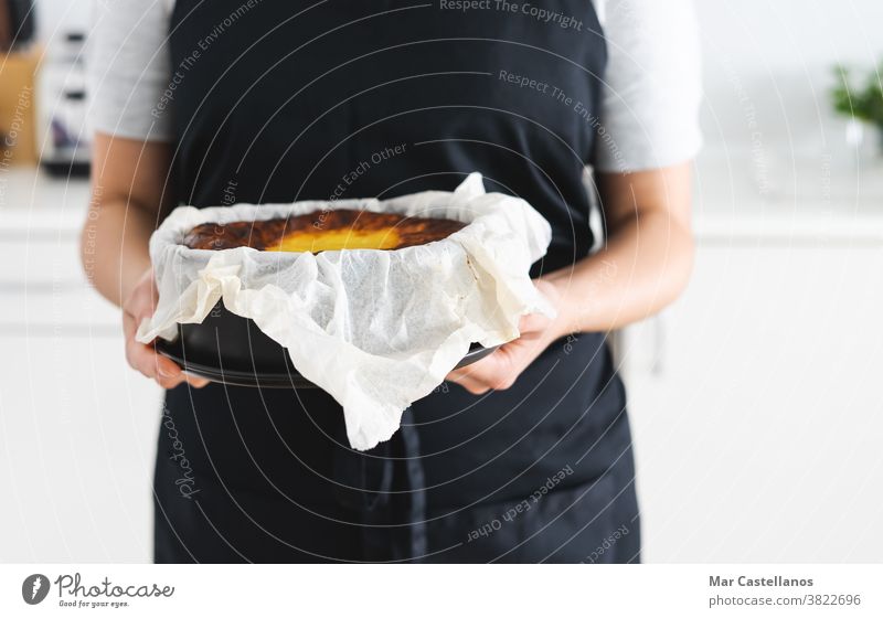 Woman in black apron showing a cheesecake. Cheesecake Copy space marble chef cook woman hands dessert sweet delicious paper kitchen pastries baked burned creamy