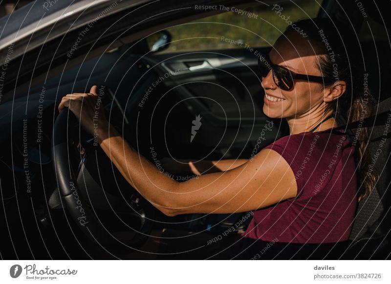 Woman in her car holding the steering wheel and smiling. drive carefree laugh happy smile joy cheerful young adult connection road trip real people vacations