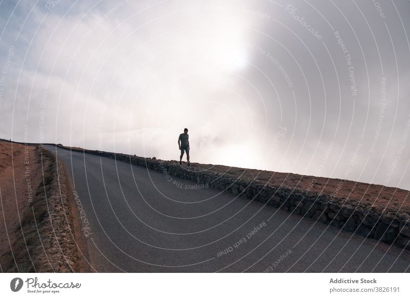 Unrecognizable traveler walking up hill along road uphill man adventure wanderlust tourist slope male empty roadway summer vacation nature trip path activity