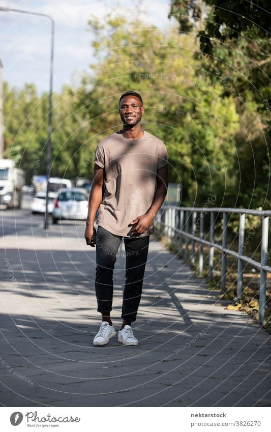 Young Black Man Walking on City Sidewalk man black smile african ethnicity sidewalk street genuine sincerity real life real people full length looking at camera