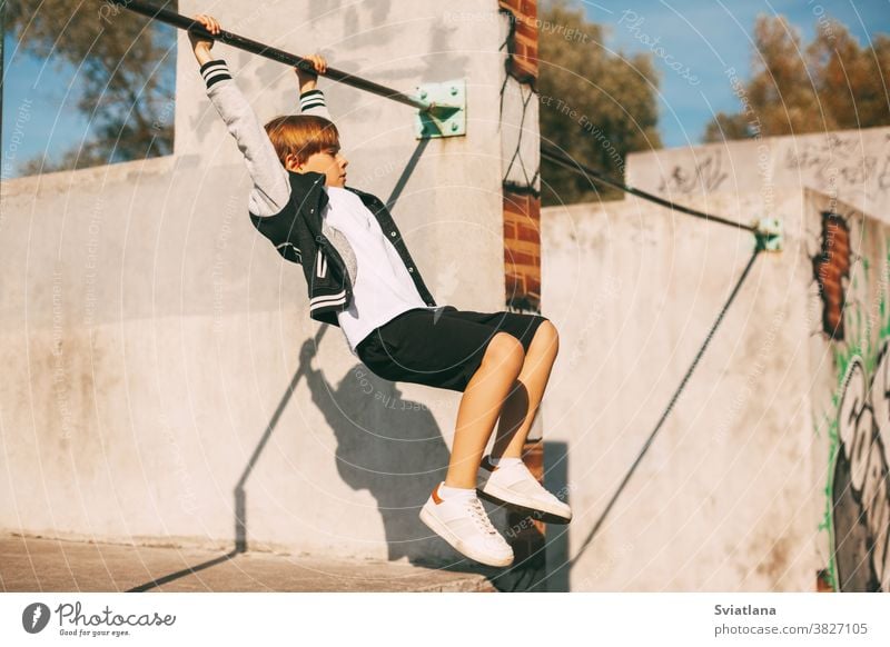 Cute boy holding hands on the horizontal bar in the Park. The boy is hanging at arm's length young sport healthy strong exercise male training athlete workout