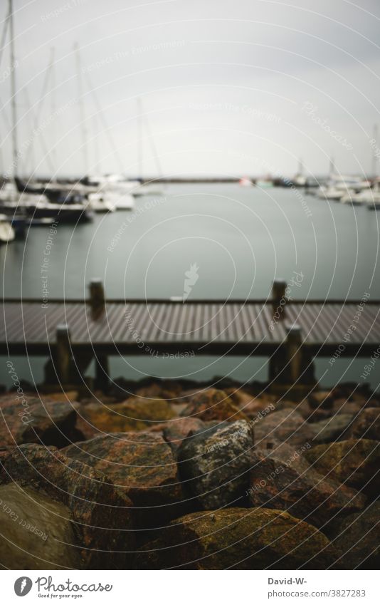 Sailing boats in rainy weather at the harbour behind a jetty that leads through the water Harbour sailboats Rainy weather Storm Ocean Footbridge stones coast