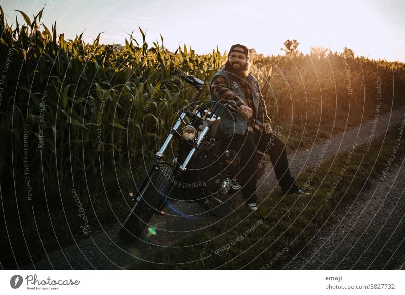 young man with beard on motorcycle in front of a cornfield at sunset teen Sunset out Field Hip & trendy Hipster Man Facial hair Motorcycle harley Maize field