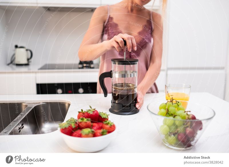 Crop woman preparing coffee for breakfast french press coffeemaker home kitchen early pajama prepare female counter silk beverage drink aromatic fresh brew