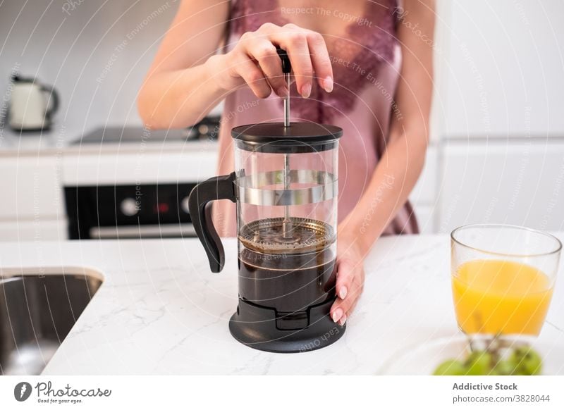 Crop woman preparing coffee for breakfast french press coffeemaker home kitchen early pajama prepare female counter silk beverage drink aromatic fresh brew