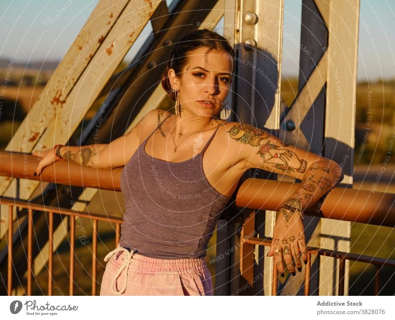 Stylish woman in tattoos standing in city style trendy bridge metal sunset summer relax rest enjoy young urban freedom delight glad evening twilight cool