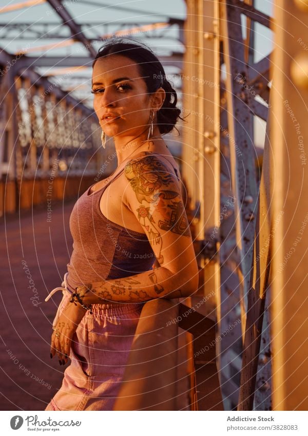 Stylish woman in tattoos standing in city style trendy bridge metal sunset summer relax rest enjoy young urban freedom delight glad evening twilight cool