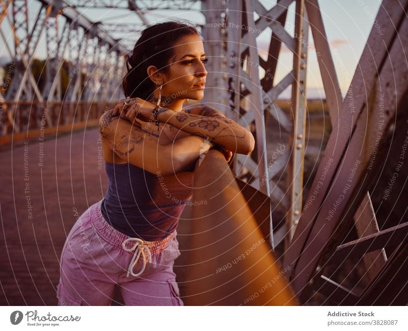 Stylish woman in tattoos standing in city style trendy bridge metal sunset summer relax rest enjoy young urban freedom delight glad evening twilight cool