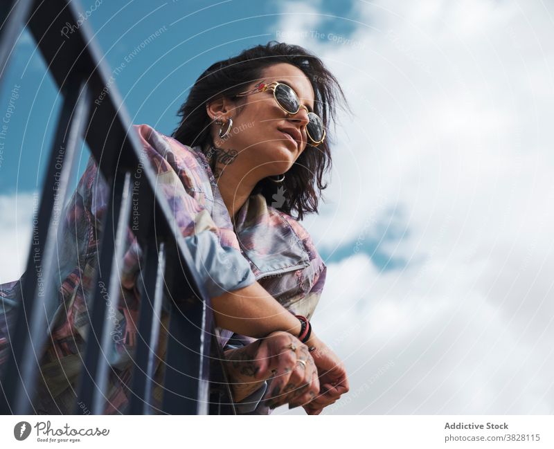 Stylish woman in tattoos standing in city street style millennial determine sunglasses accessory young independent female metal fence fashion relax