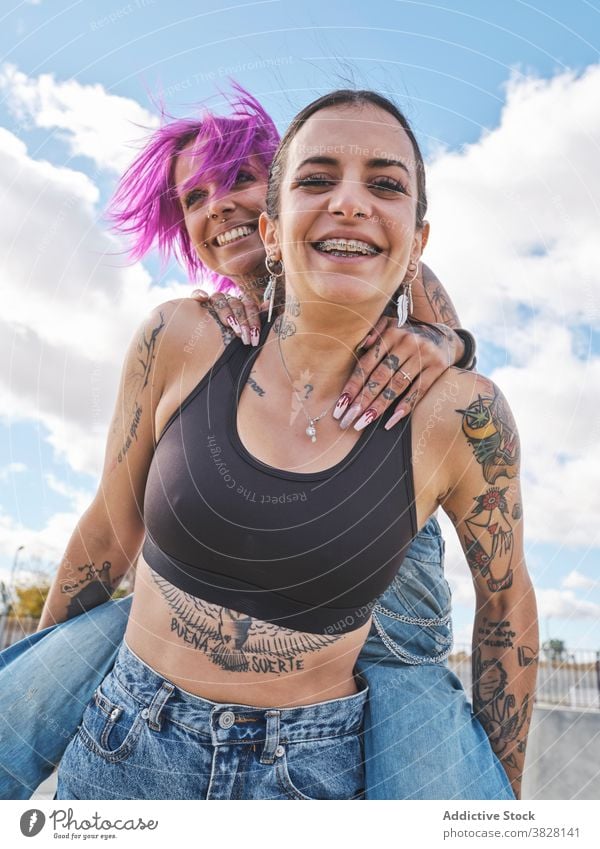 Cheerful women having fun together in skate park piggyback friend friendship informal tattoo subculture cool delight laugh optimist weekend happy joy carefree