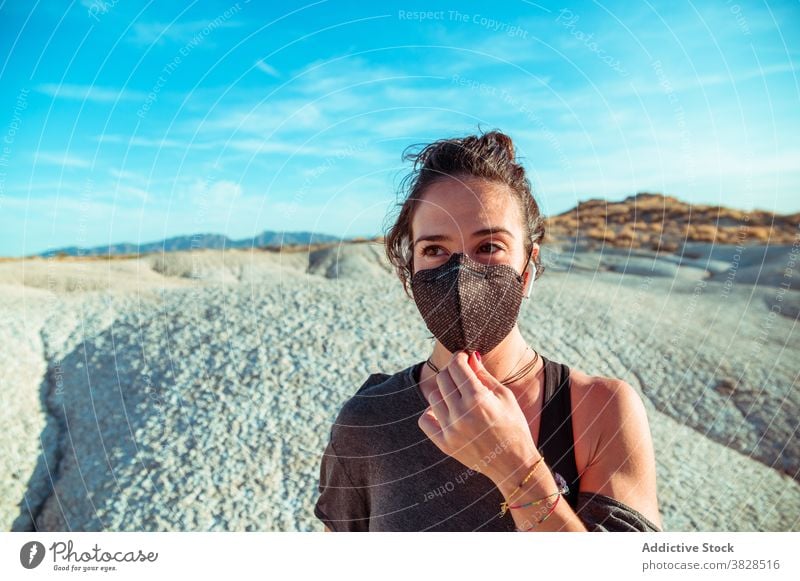 Sporty woman in mask and earphones standing among dry terrain sportswoman earbuds desert confident listen protect wireless strong determine coronavirus covid 19