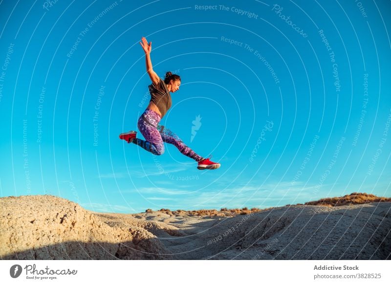 Strong sportswoman jumping over sandy hill fly skyline blue sky desert rough active energy leap athlete slope terrain nature workout training exercise female