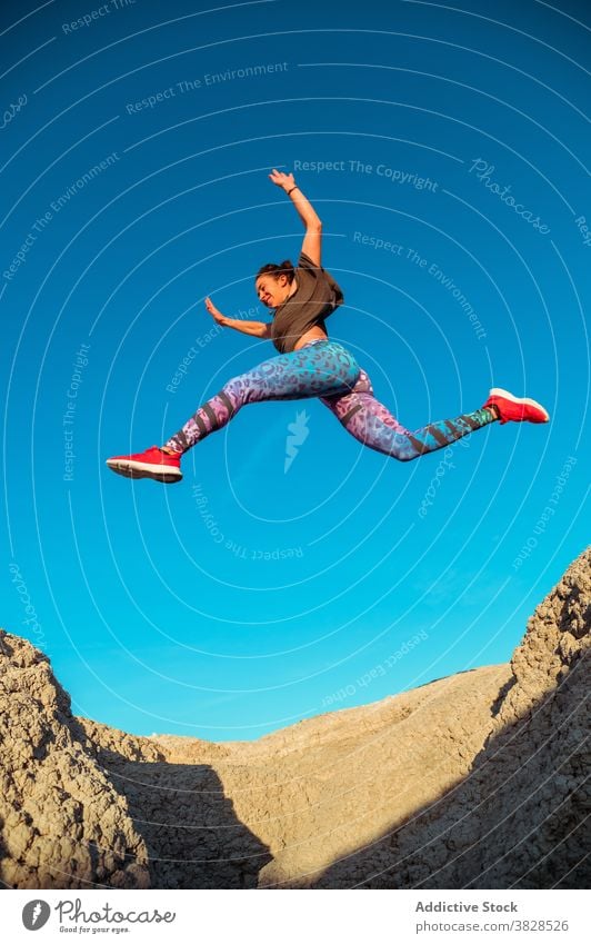 Strong sportswoman jumping over sandy hill fly skyline blue sky desert rough active energy leap athlete slope terrain nature workout training exercise female