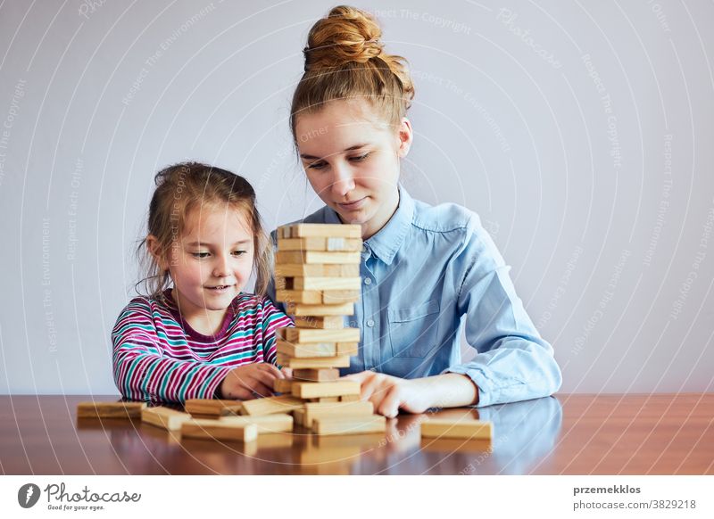 Little girl preschooler and her elder sister playing together with wooden blocks game toy activity brick build child childhood concept construction copy space