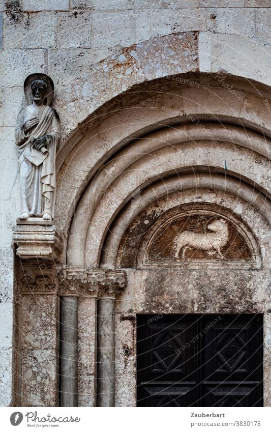 Lamb as relief and statue of a saint on a Romanesque church portal with round arch Relief holier Statue Church Portal Round arch Old religion religious worship