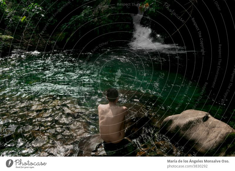 A man sitting on a rock in front of a green water well of a river in the jungle. Lifestyle Nature reserve nature conservation nature park nature lovers