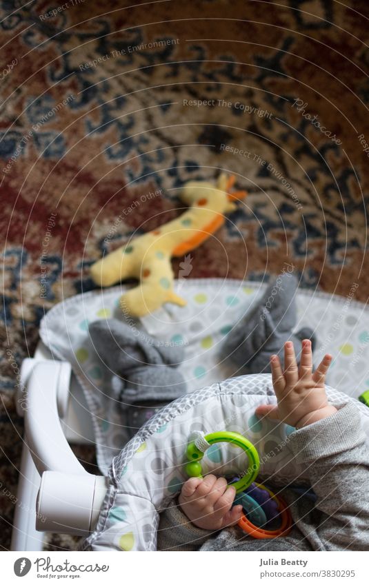 Baby seated with toys on orange rug; reaching towards giraffe toy baby infant child 0 - 12 months infancy childhood plastic rings booties drop object permanence