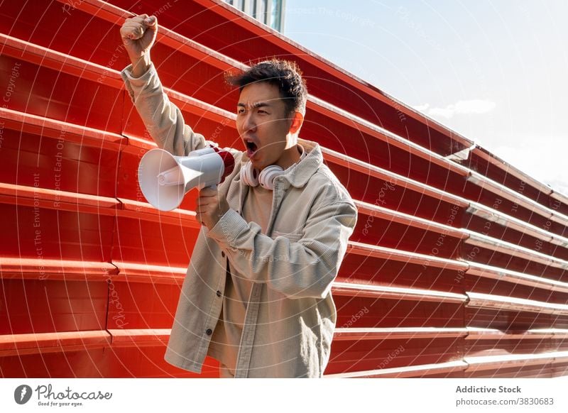 Emotional Asian man shouting in loudspeaker and raising fist scream megaphone rebel revolutino emotional overwhelmed agitate fist up provocation gesture