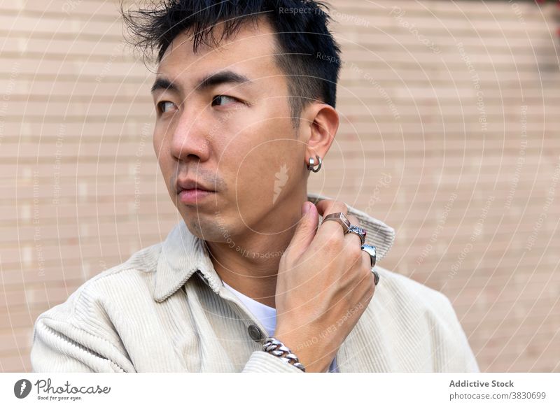 Pondering Asian man standing with eyes closed against brick wall ponder calm unemotional touch lapel thoughtful serious masonry pensive think casual contemplate