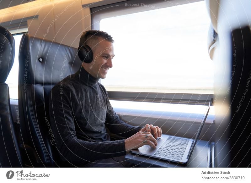 Man in headphones working on laptop in train business trip man freelance remote typing travel male seat modern passenger gadget device young netbook guy journey