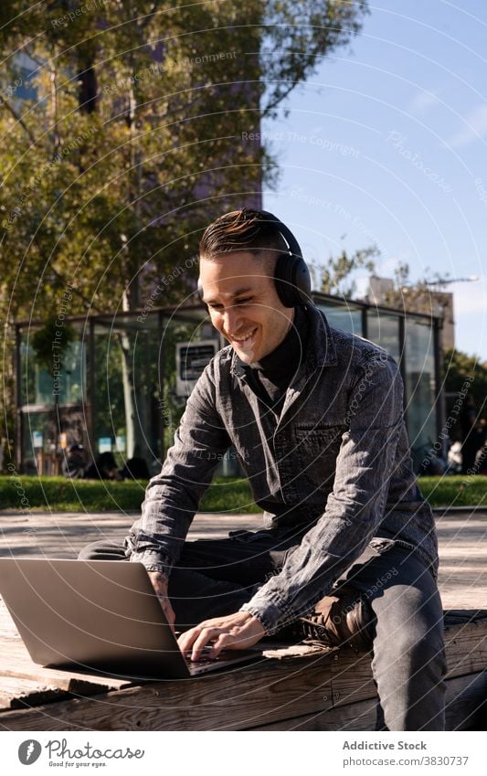 Cheerful young man working on laptop in headphones using typing cheerful internet freelance browsing occupation male remote device modern surfing business