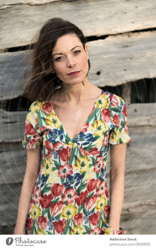 Thoughtful woman next to old wooden construction thoughtful wall style fashion dreamy exterior pensive slender female shorts hand in pocket shirt dark hair