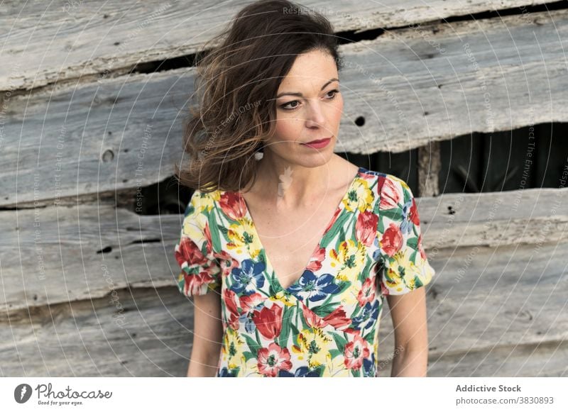 Thoughtful woman next to old wooden construction thoughtful wall style fashion dreamy exterior pensive slender female shorts hand in pocket shirt dark hair