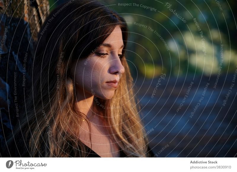 Serious pensive woman standing near tree sad silent thoughtful alone lonely serious upset melancholy think unhappy problem depression mood female young trunk